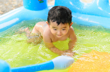 Asian kid playing in inflatable baby swimming pool on hot summer day.