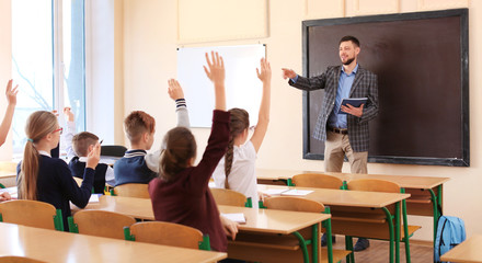 Pupils listening teacher and raising hands to answer in classroom