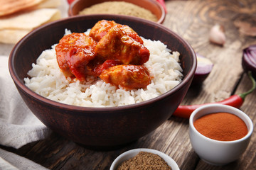 Bowl with delicious chicken tikka masala, rice and spices on table