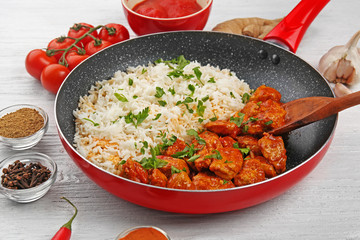 Frying pan with tasty chicken tikka masala and rice on wooden table