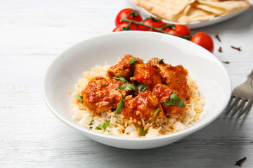 Plate with tasty chicken tikka masala and rice on wooden table