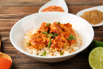 Plate with tasty chicken tikka masala, rice and spices on wooden table