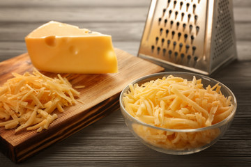 Bowl and wooden board with grated cheese on table
