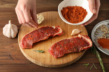 Woman preparing tasty steaks on wooden board