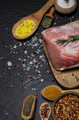 Raw pork meat on a cutting board with rosemary and spices.