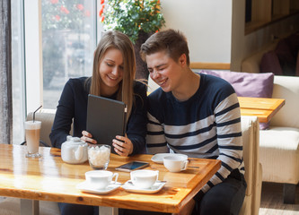 Cheerful couple dating in a cafe. They are having fun and smiling with tablet.  Dating, love, romanic, dating, lifestyle, study, education. Natural emotion
