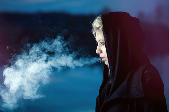 Young female exhaling smoke in black