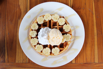 Ice cream on honey waffle with banana on white plate.