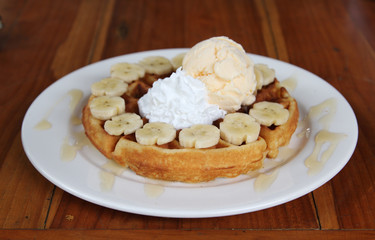 Ice cream on honey waffle with banana on white plate.