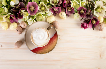 Coffee cup cappuccino with spring flowers and Easter egg on light wooden background. Top view, text space.