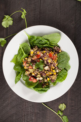 Spinach Bean Quinoa Salad with corn and tomatoes on white plate with dark wooden background above shot