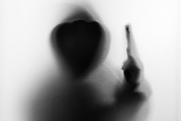 Obraz premium Shadow blur of horror man in jacket with hood gun in his hand.Dangerous man behind the frosted glass.Mystery man.Halloween background.Black and white picture.Blur picture.