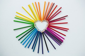Colored pencils arranged in heart shape on white background