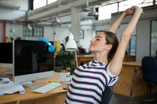 Female graphic designer sitting on chair and stretching her arms - Powered by Adobe