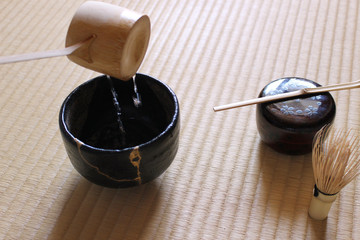 日本の畳の上に置かれた金継された抹茶の茶碗に湯を注ぐ