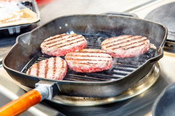 Beef burgers are fried on a frying pan grill.