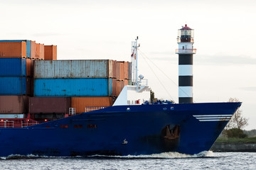 Blue container ship's bow against big lighthouse, Latvia