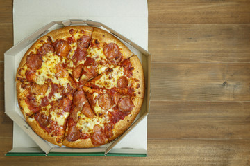 Pizza pepperoni in paper box on brown wooden background