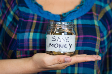 Woman facing camera, holding glass jar with coins inside, label reading save money