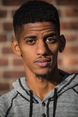 Fototapeta premium A young, black man poses infront of a red brick wall in NYC