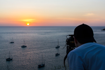 Person shooting sunset and boats. Back view of a person shooting the sunset and sailing boats. Horizontal outdoors shot.