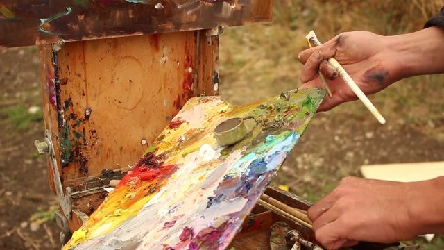 Painting Outdoors. Artist Working En Plein Air. Oil Paints On A Palette. The artist tidies tools