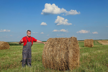 Naklejka na ściany i meble Farmer and bale of hay in field, gesturing with thumb up