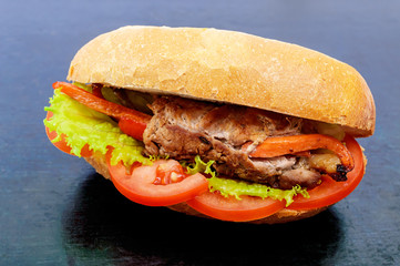 Sandwich: Meat rolls with vegetables in a bun with tomato and lettuce leaves on the black background.