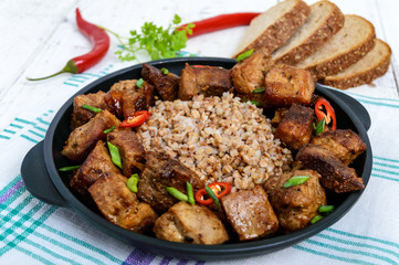 Buckwheat porridge with pieces of fried pork, served on a cast-iron frying pan.
