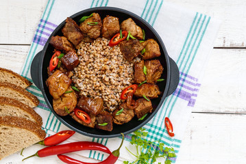 Buckwheat porridge with pieces of fried pork, served on a cast-iron frying pan.