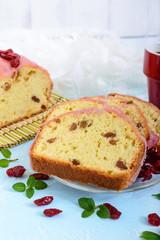 Soft festive fruitcake with raisins and dried cranberries, decorated with sugar icing cut by pieces and cup of coffee on a light background. Vertical view
