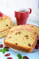 Soft festive fruitcake with raisins and dried cranberries, decorated with sugar icing cut by pieces and cup of coffee on a light background. Vertical view