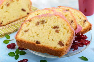 Soft festive fruitcake with raisins and dried cranberries, decorated with sugar icing cut by pieces and cup of coffee on a light background.