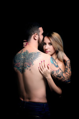 Sexy woman hugging tattooed man on black background