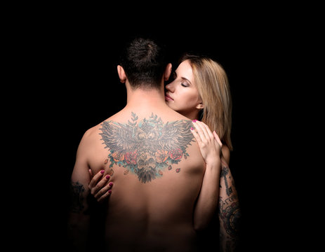 Sexy woman hugging tattooed man on black background