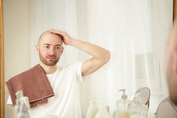 Hair loss concept. Young handsome man looking at mirror