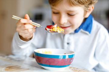 little blond school kid boy eating cereals with milk and berries, fresh strawberry for breakfast