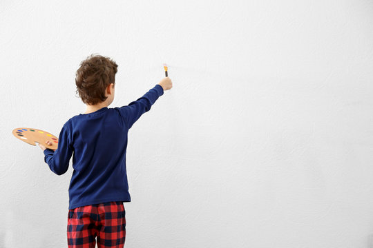 Cute little boy painting on light wall