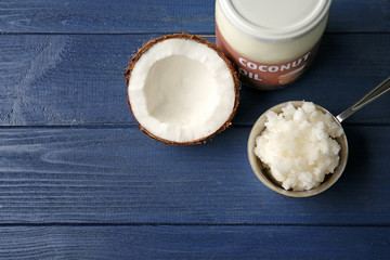 Metal scoop with fresh coconut oil taken from glass jar on wooden background