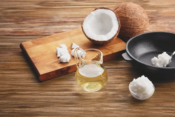 Glass jug with coconut oil and kitchenware on wooden background