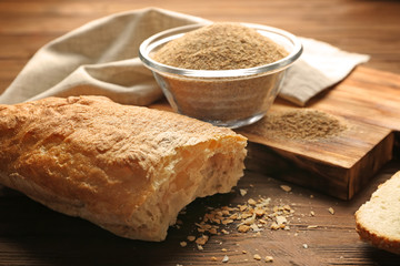 Glass bowl of bread crumbs and broken loaf on wooden table