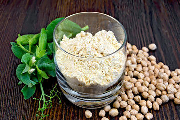 Flour chickpeas in glassful with peas on dark board