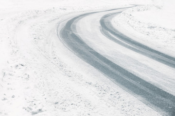 Traces of tires on snow covered road bend in winter time