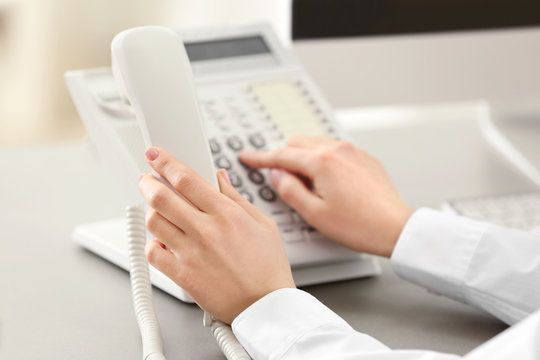 Hands of woman dialing number on telephone in office