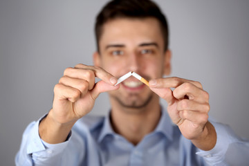 Quit smoking concept. Man breaking cigarette, on light background