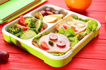 Funny sandwiches in lunch box on red wooden background