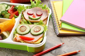 Funny sandwiches in lunch box and colorful stationery on wooden background