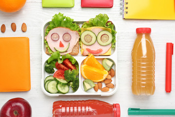 Funny sandwiches in lunch box and stationery on white wooden background