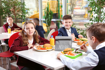 Children sitting at cafeteria table while eating lunch