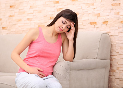 Beautiful pregnant woman suffering from headache sitting on couch